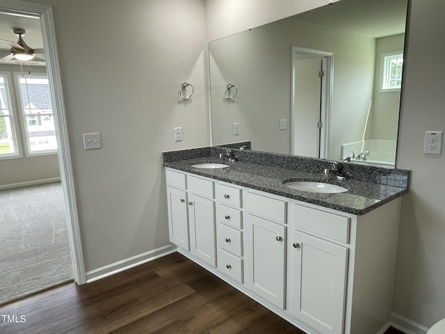 full bath with baseboards, ceiling fan, a sink, and wood finished floors