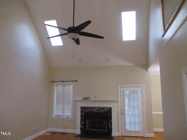 unfurnished living room featuring hardwood / wood-style floors, a skylight, high vaulted ceiling, a high end fireplace, and ceiling fan