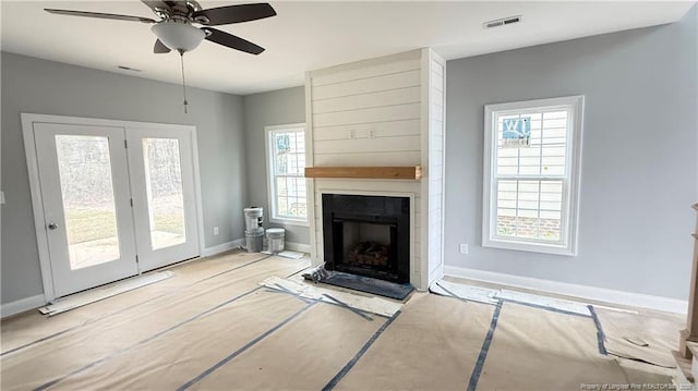 unfurnished living room with a ceiling fan, a large fireplace, visible vents, and baseboards