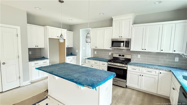 kitchen with light wood finished floors, tasteful backsplash, appliances with stainless steel finishes, a center island, and white cabinetry