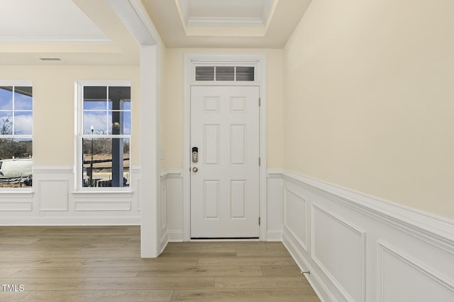 entryway with ornamental molding, light wood-type flooring, and a raised ceiling