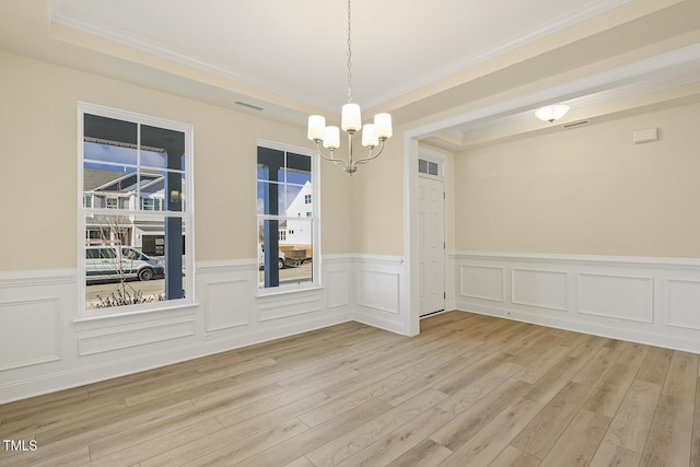 unfurnished dining area with light wood-type flooring, an inviting chandelier, a tray ceiling, and crown molding