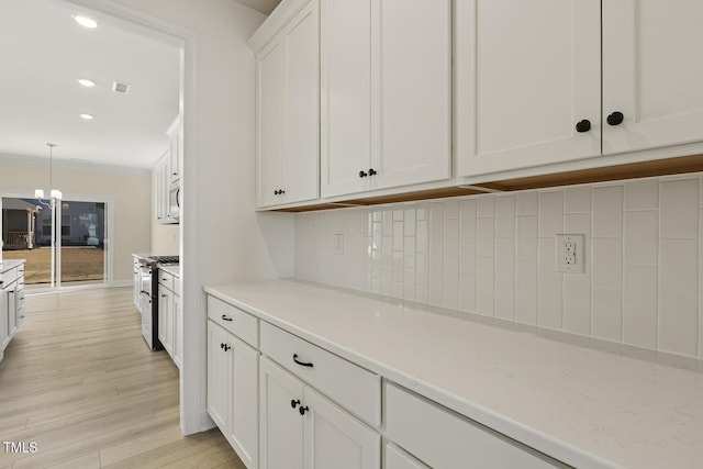 kitchen featuring decorative light fixtures, white cabinetry, stainless steel gas range, light wood-type flooring, and crown molding