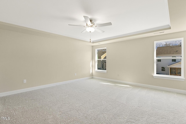 carpeted spare room with ceiling fan, plenty of natural light, and a tray ceiling