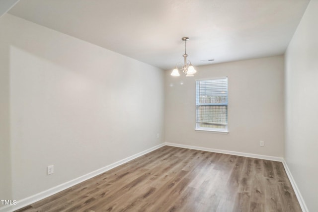 spare room featuring hardwood / wood-style flooring and a chandelier