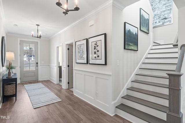 entrance foyer featuring crown molding, stairway, wainscoting, wood finished floors, and a chandelier