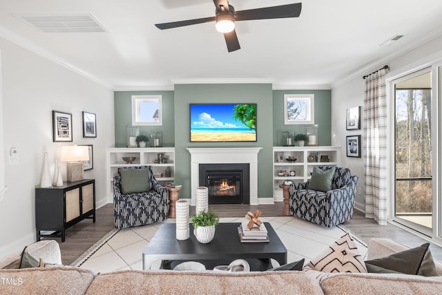 tiled living room with baseboards, a glass covered fireplace, visible vents, and crown molding