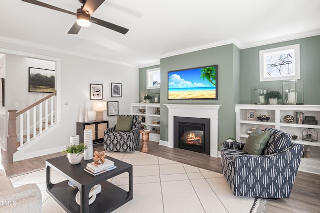 living room with a glass covered fireplace, wood finished floors, crown molding, and stairs