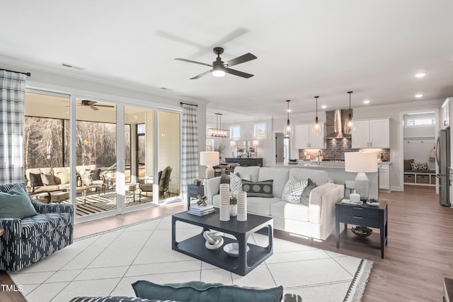 living area with recessed lighting, visible vents, ornamental molding, light wood-type flooring, and ceiling fan with notable chandelier