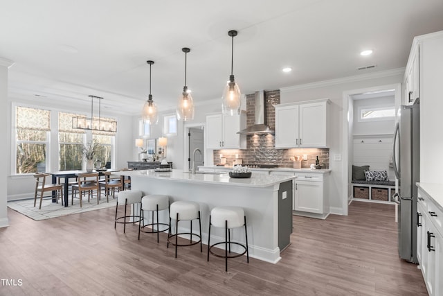 kitchen with a sink, a kitchen breakfast bar, wall chimney range hood, freestanding refrigerator, and decorative backsplash