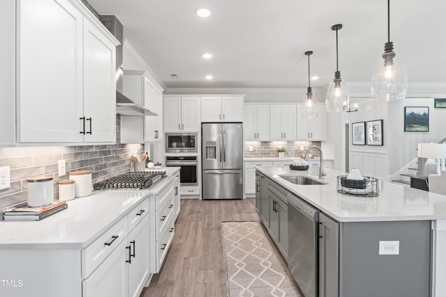 kitchen featuring stainless steel appliances, a sink, white cabinetry, wall chimney exhaust hood, and crown molding