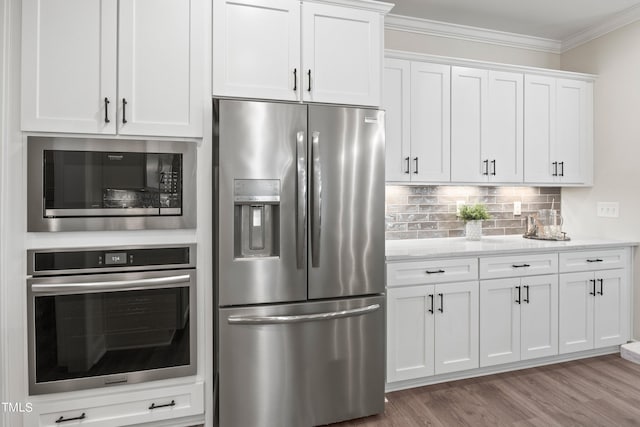 kitchen with light wood-style flooring, white cabinetry, ornamental molding, appliances with stainless steel finishes, and decorative backsplash