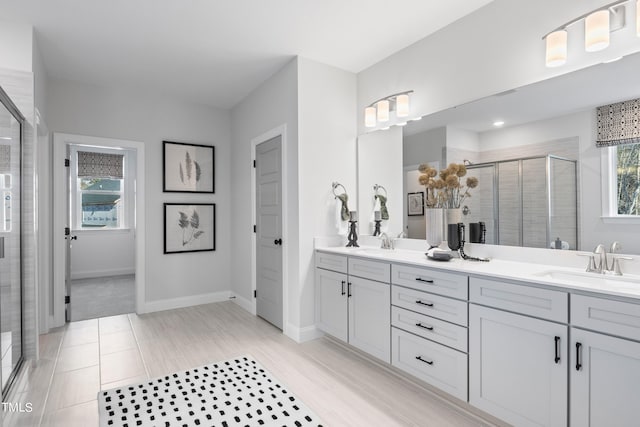 bathroom with a stall shower, a sink, baseboards, and double vanity