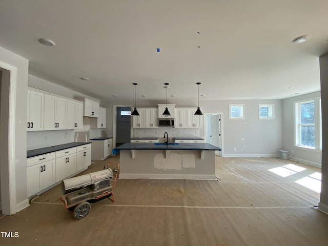 kitchen featuring a sink, white cabinetry, baseboards, stainless steel microwave, and dark countertops