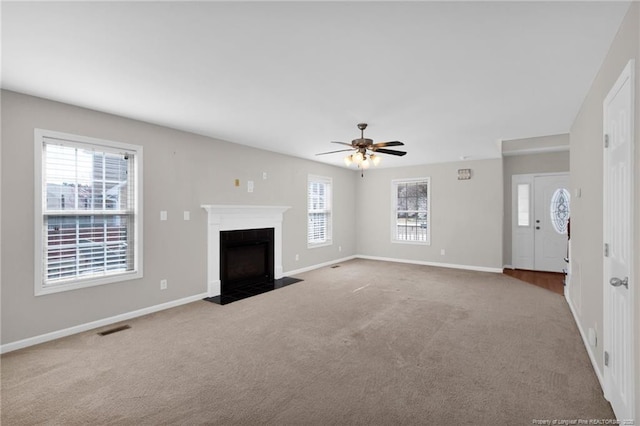 unfurnished living room featuring light carpet, a fireplace with flush hearth, visible vents, and a wealth of natural light