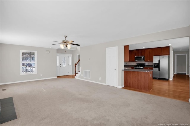 unfurnished living room featuring light colored carpet, visible vents, baseboards, and stairs