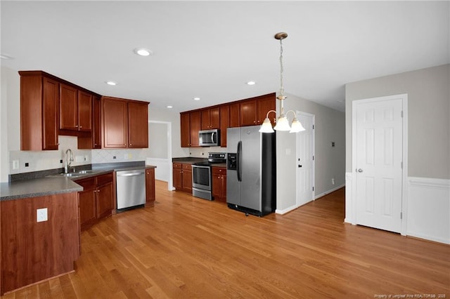 kitchen featuring dark countertops, decorative light fixtures, stainless steel appliances, light wood-type flooring, and a sink