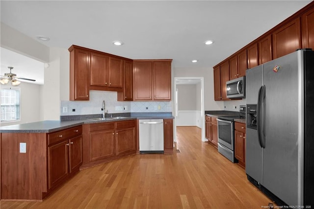 kitchen featuring stainless steel appliances, dark countertops, a sink, and light wood-style flooring