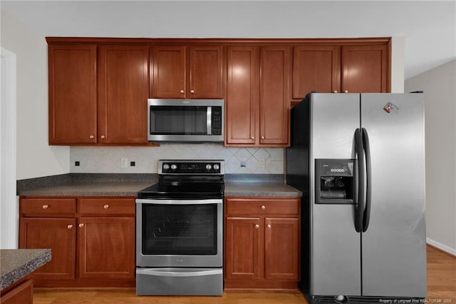 kitchen featuring brown cabinetry, decorative backsplash, dark countertops, light wood-style flooring, and stainless steel appliances