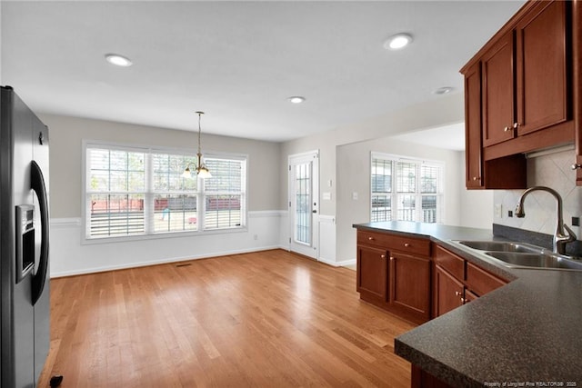 kitchen with stainless steel refrigerator with ice dispenser, a wealth of natural light, dark countertops, hanging light fixtures, and a sink