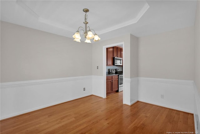 empty room with baseboards, light wood-type flooring, a raised ceiling, and an inviting chandelier