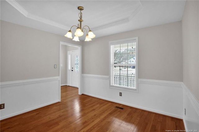 unfurnished dining area featuring wood finished floors, a raised ceiling, visible vents, and a notable chandelier