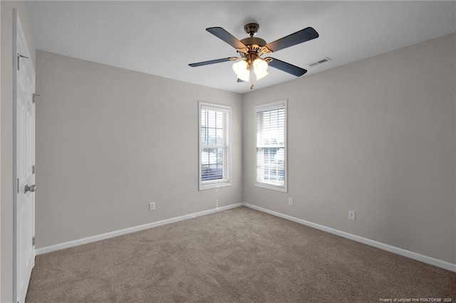 spare room with light colored carpet, visible vents, ceiling fan, and baseboards