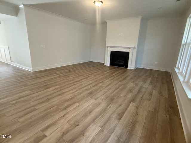 unfurnished living room featuring ornamental molding, a fireplace, baseboards, and wood finished floors