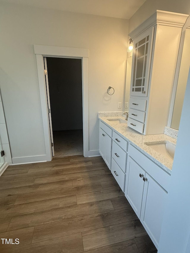 full bathroom featuring double vanity, wood finished floors, a sink, and baseboards