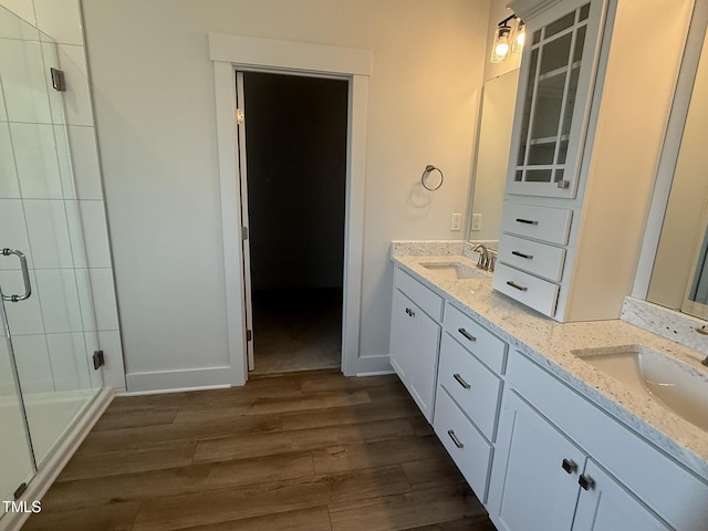 full bathroom featuring a stall shower, double vanity, a sink, and wood finished floors