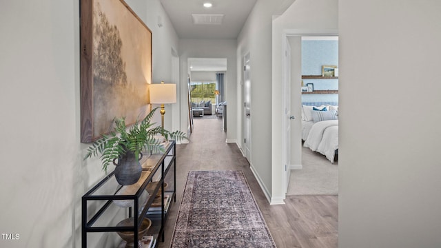 hall featuring baseboards, visible vents, and wood finished floors