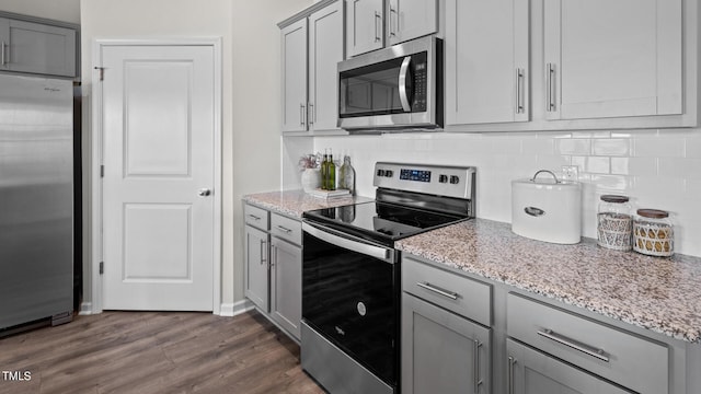 kitchen featuring appliances with stainless steel finishes, gray cabinets, dark hardwood / wood-style flooring, and light stone counters