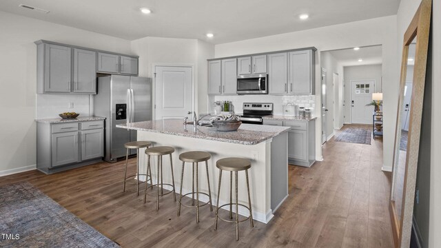 kitchen featuring gray cabinets, dark wood-type flooring, a kitchen breakfast bar, a center island with sink, and appliances with stainless steel finishes