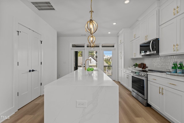 kitchen featuring light hardwood / wood-style floors, stainless steel appliances, an island with sink, hanging light fixtures, and white cabinetry