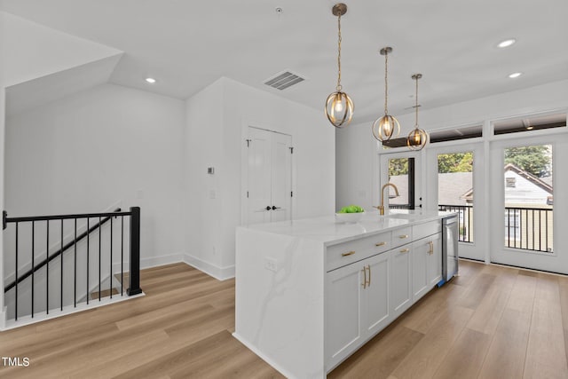 kitchen with light stone countertops, a kitchen island with sink, hanging light fixtures, and white cabinetry