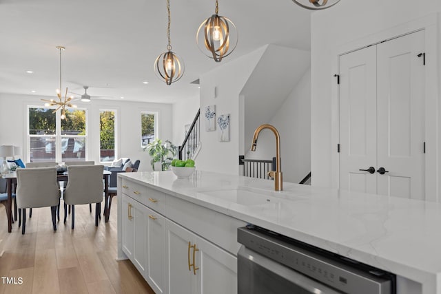 kitchen featuring sink, white cabinetry, stainless steel dishwasher, hanging light fixtures, and light stone countertops