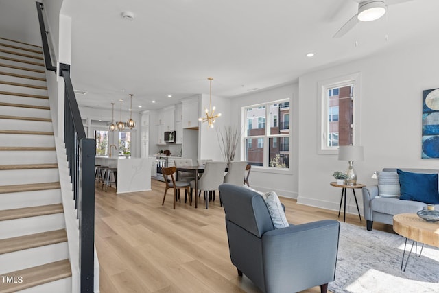 living room with ceiling fan with notable chandelier, light wood-type flooring, and sink