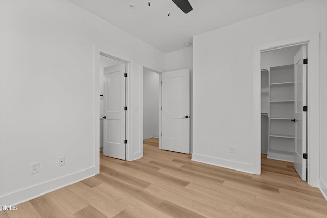 unfurnished bedroom with a closet, light wood-type flooring, ceiling fan, and a spacious closet