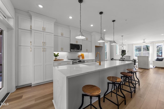 kitchen featuring white cabinetry, an island with sink, hanging light fixtures, stainless steel appliances, and sink