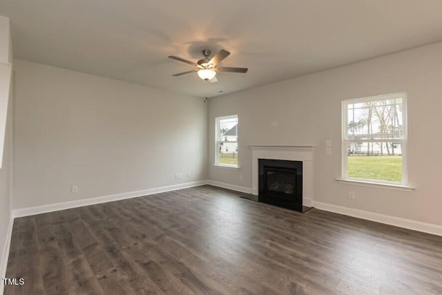 unfurnished living room with a glass covered fireplace, dark wood-style flooring, ceiling fan, and baseboards