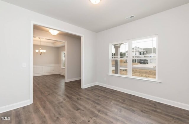 empty room with visible vents, a wainscoted wall, dark wood-type flooring, a tray ceiling, and a chandelier