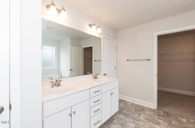 full bath with double vanity, baseboards, a walk in closet, and a sink