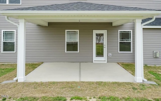 doorway to property with a shingled roof, a lawn, and a patio