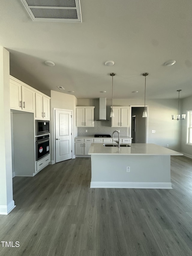 kitchen with white cabinets, light countertops, wall chimney range hood, built in microwave, and a center island with sink