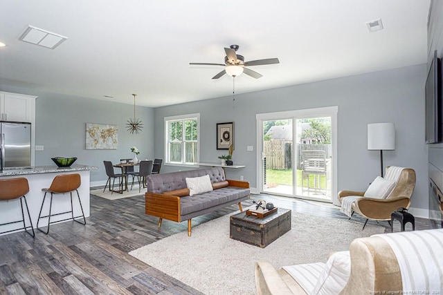 living area featuring plenty of natural light, visible vents, dark wood-type flooring, and a ceiling fan