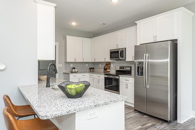 kitchen with light wood-style flooring, a peninsula, a kitchen bar, stainless steel appliances, and tasteful backsplash