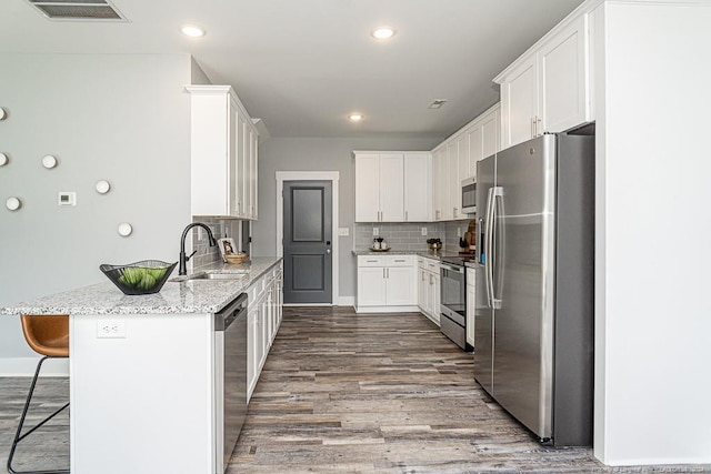 kitchen with a sink, white cabinets, a kitchen bar, and appliances with stainless steel finishes
