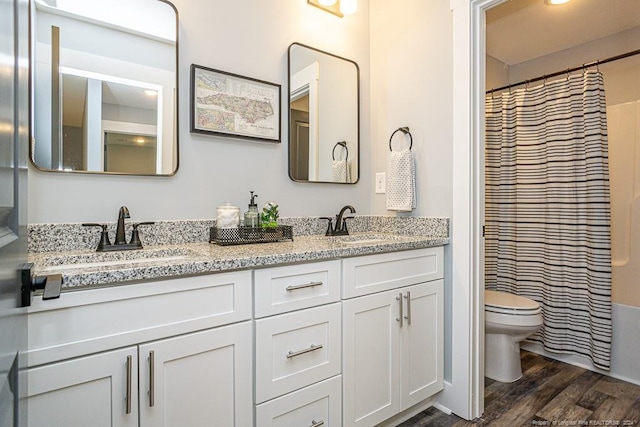 full bath featuring double vanity, a sink, toilet, and wood finished floors