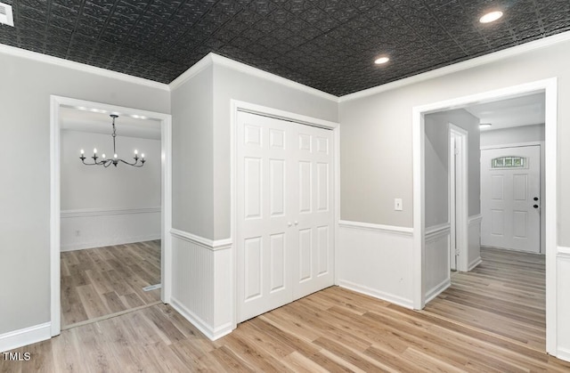 hall with an ornate ceiling, a chandelier, light wood-style flooring, and crown molding