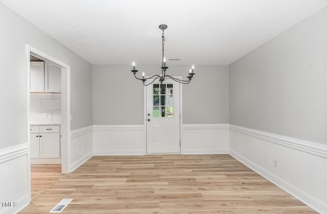 unfurnished dining area featuring light wood-type flooring, visible vents, a notable chandelier, and wainscoting